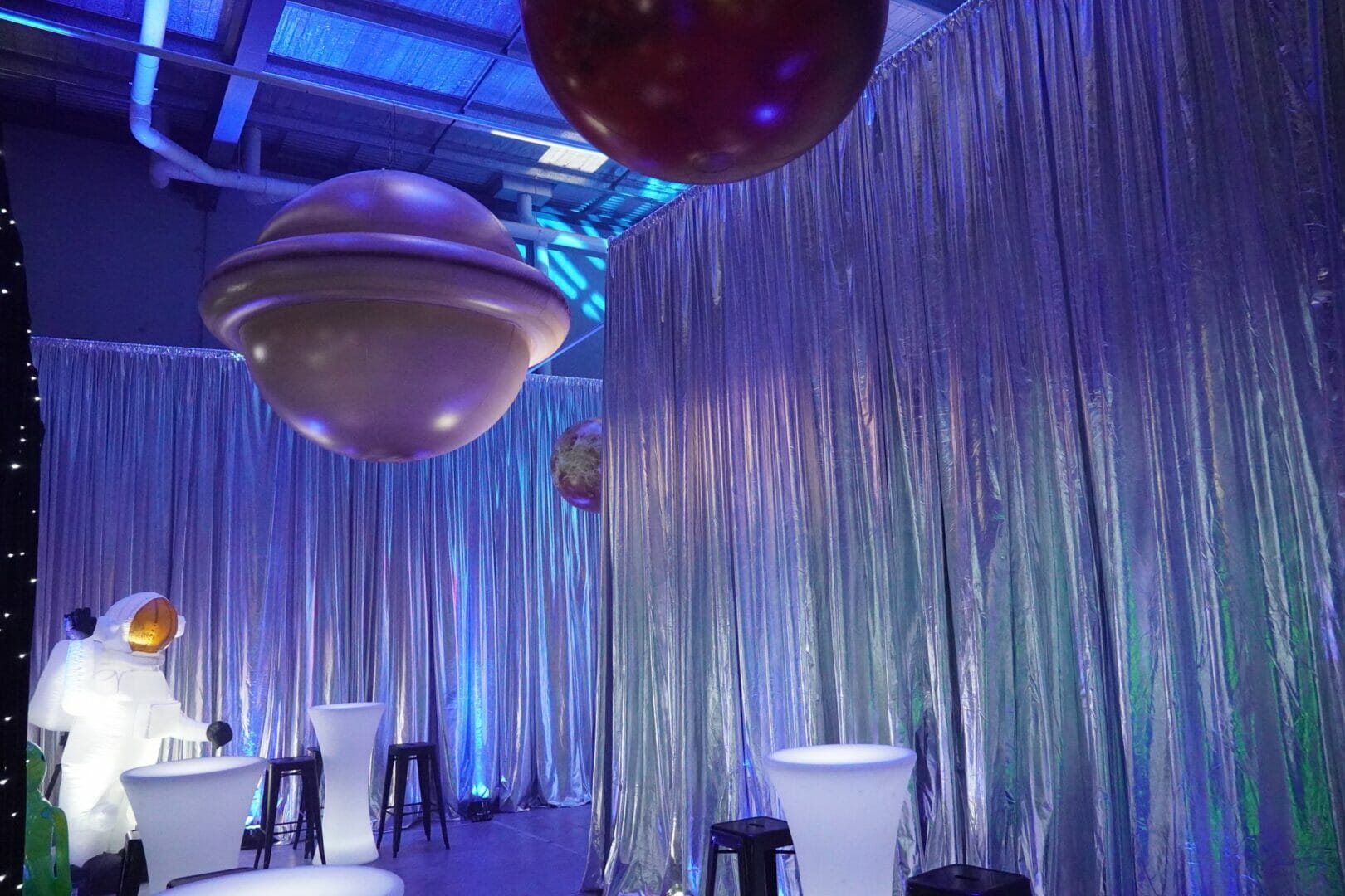 Silver metallic drape, inflatable planets, illuminated bar tables, and bar stools in a space themed party setup
