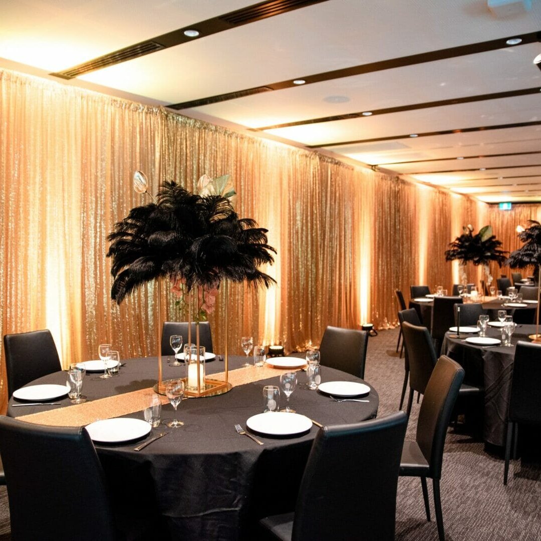 Gold sequin drape, black feather centerpieces, and table setups at puffing bill event space setup