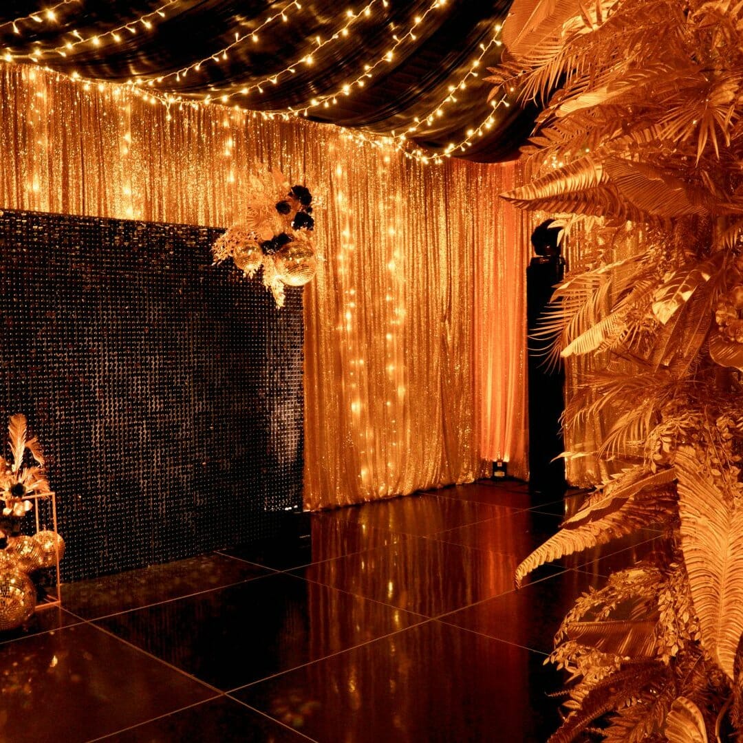 gold leaf centrepiece, gold sequin drape, fairy lights, sequin panel backdrop, and gold centrepieces in black & gold themed setup