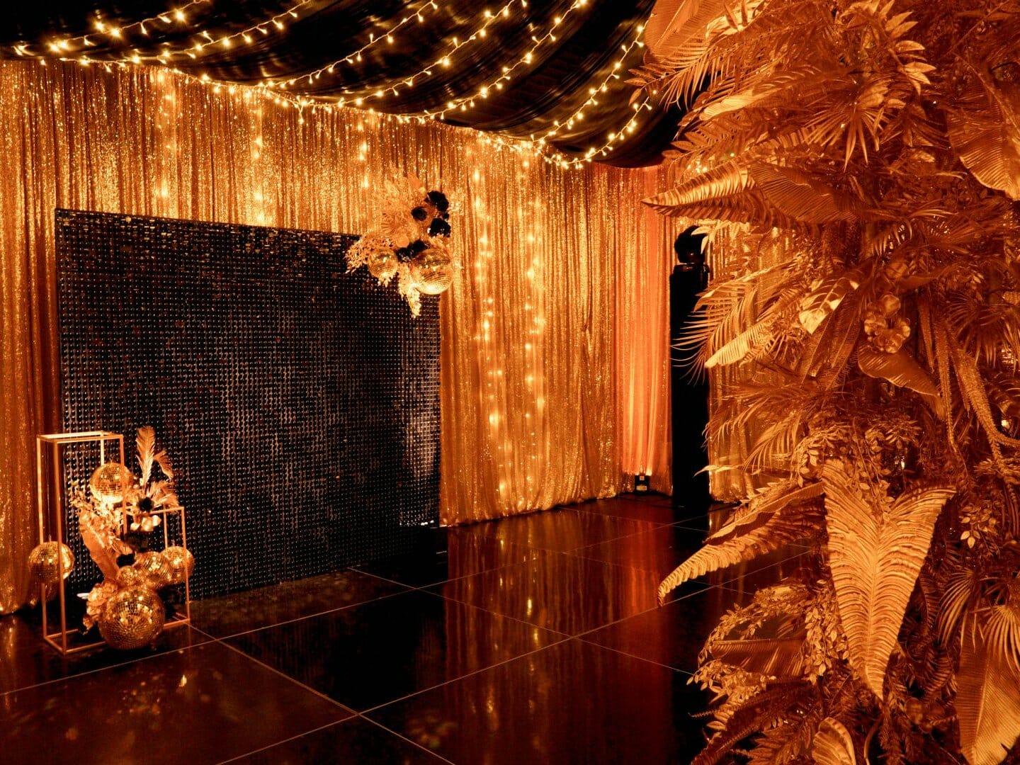 gold leaf centrepiece, gold sequin drape, fairy lights, sequin panel backdrop, and gold centrepieces in black & gold themed setup