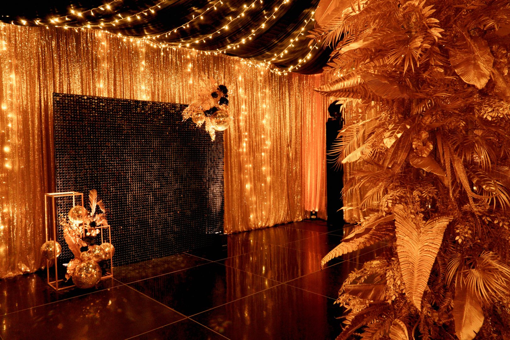 gold leaf centrepiece, gold sequin drape, fairy lights, sequin panel backdrop, and gold centrepieces in black & gold themed setup