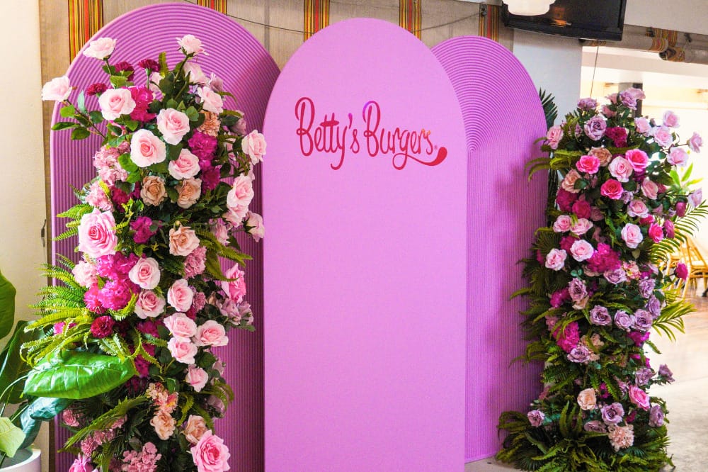 Product launches Betty's Burgers decal on pink rounded arches with floral pillars on either side