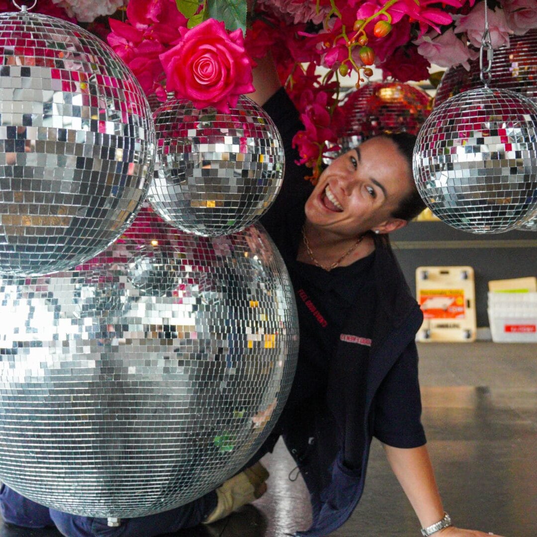 Emma setting up a pink floral and sliver mirror ball ceiling installation